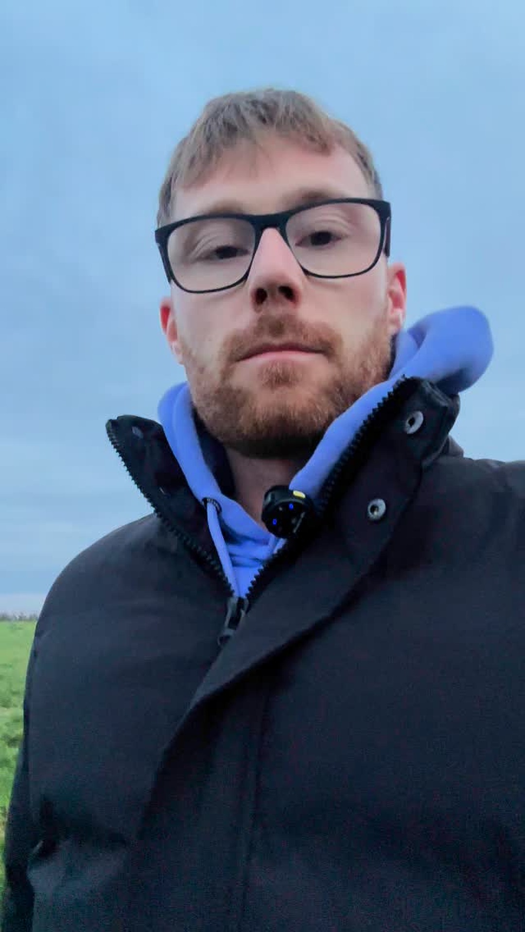 Kelvin outdoors in a dark jacket, looking straight into the lens against a clear sky.